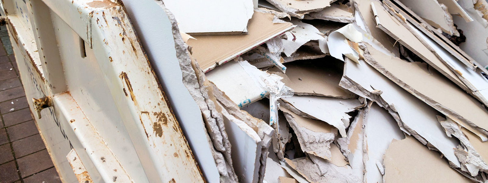 in a waste container stacks sheets of plasterboard for their disposal